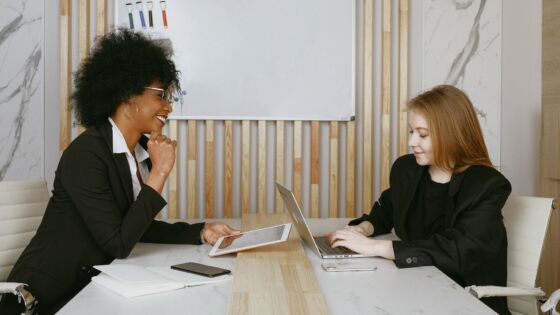 two women sitting at a table with a laptop