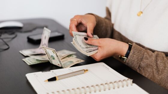 a woman holding a stack of money next to a notebook