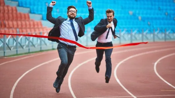 a couple of men running across a race track